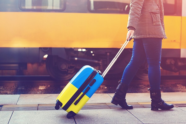 Bahnreisende mit Koffer in Farben der ukrainischen Flagge.